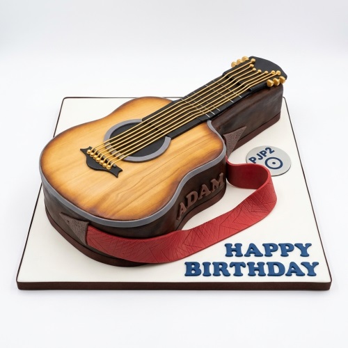 3D acoustic guitar shaped birthday cake with red strap and 'Happy Birthday' message on a white board.