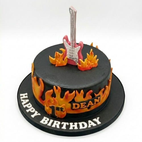 Round black cake with a red electric guitar topper and orange flames, with a custom age and message.