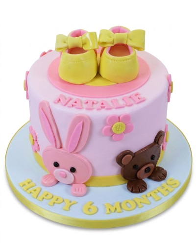 Pink baby celebration cake with yellow booties, bunny, teddy bear, and flowers.