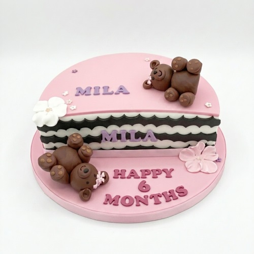 Round pink cake with two brown teddy bears, white and pink flowers, and black and white stripes.
