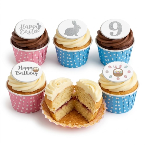 Assortment of kids birthday cupcakes with white and brown frosting, pink and blue polka dot wrappers, and edible toppers including a glittery number 9, bunny, and 'Happy Birthday' message.