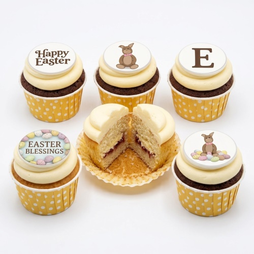 Assortment of Easter themed cupcakes with white frosting, yellow polka dot wrappers, and edible toppers featuring bunnies, mini eggs, and "Happy Easter" messages.