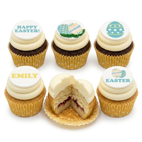Six Easter cupcakes with white frosting and decorative Easter egg toppers. One cupcake is cut open revealing a jam filling.