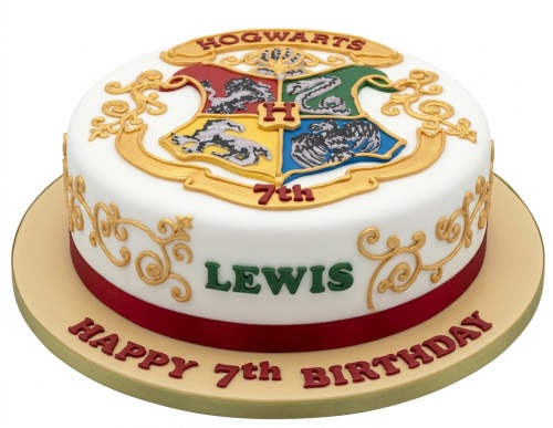 Round white fondant cake with a gold and coloured Hogwarts crest, gold scrollwork, and a red ribbon.