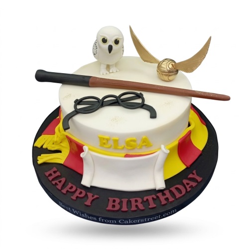 Two-tier Harry Potter theme birthday cake with Hedwig, Golden Snitch, wand, and glasses.
