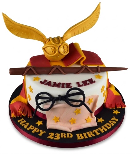 Round white Harry Potter themed birthday cake with Golden Snitch, wand, glasses, and red and yellow scarf.
