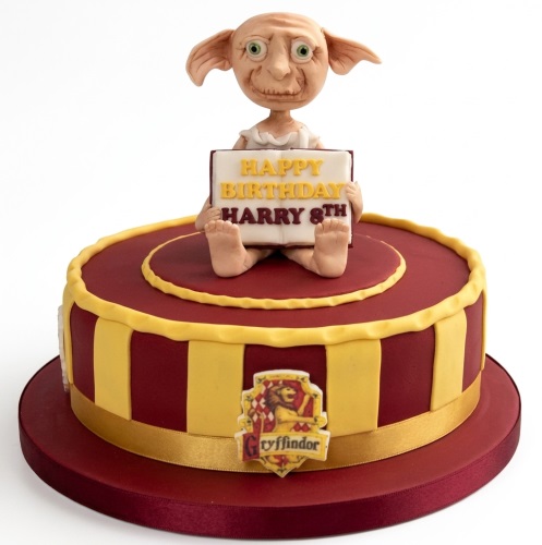 Round Harry Potter cake with Dobby figurine, Gryffindor emblem, and custom birthday message.