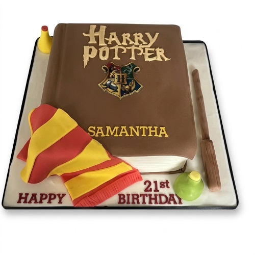 Harry Potter themed birthday cake shaped like a book with Hogwarts crest, scarf, wand, and potion bottle.