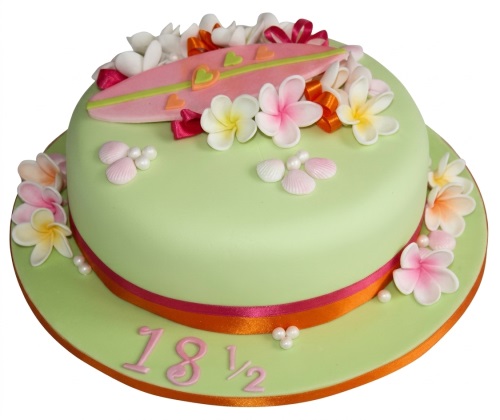 Round light green cake with pink surfboard, tropical flowers, and edible seashells.