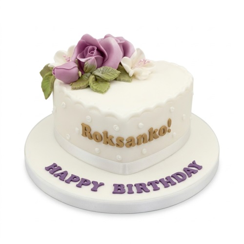 Heart-shaped white birthday cake with purple sugar roses, white flowers, green leaves, and a personalised message.