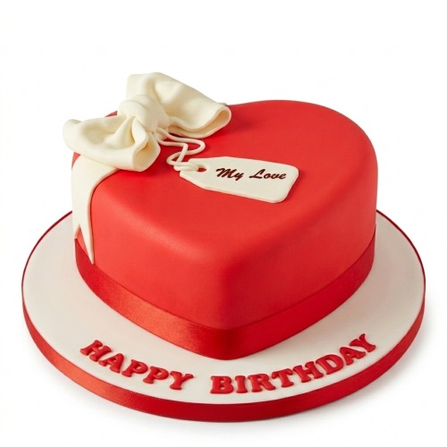 Red heart-shaped birthday cake with a white bow and "My Love" tag on a white cake board with "Happy Birthday".