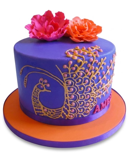 Round purple cake with gold peacock design, pink and orange sugar flowers, and orange board.