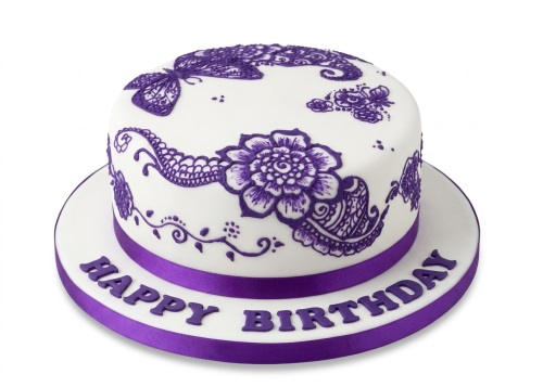 Round white birthday cake with intricate purple henna-style floral and butterfly decorations, with 'Happy Birthday' on the board.
