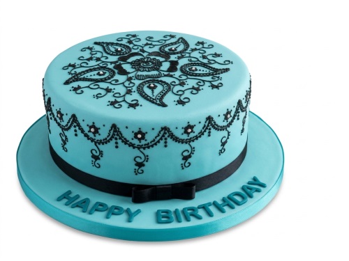 Round teal birthday cake with intricate black mehndi-style piping and a black ribbon.