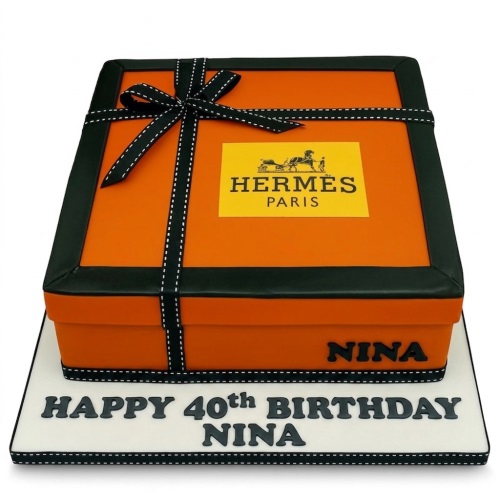 Orange and black Hermes gift box birthday cake with black ribbon and logo, on a white board.