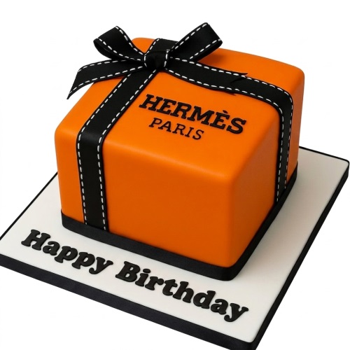 Square orange cake designed as a Hermes style gift box with black ribbon and bow, and 'Happy Birthday' message on the board.
