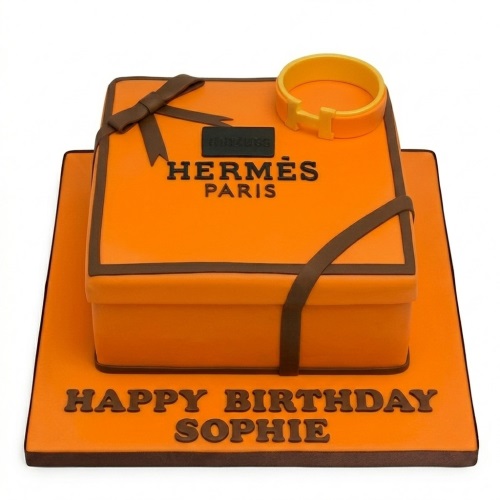 Orange Hermes gift box birthday cake with brown ribbon and bracelet, 'Happy Birthday' message.