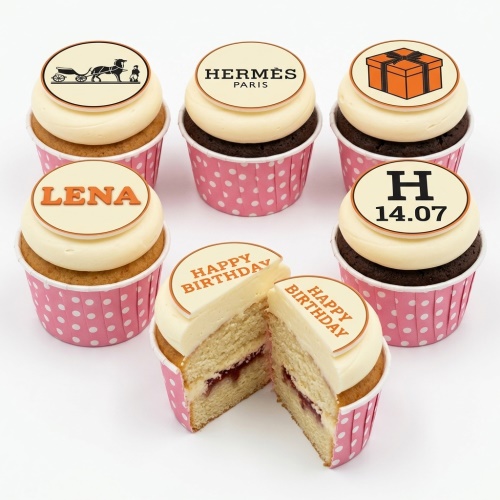 Set of Hermes inspired birthday cupcakes with designer logos, gift box, and personalised message toppers in pink polka dot wrappers.