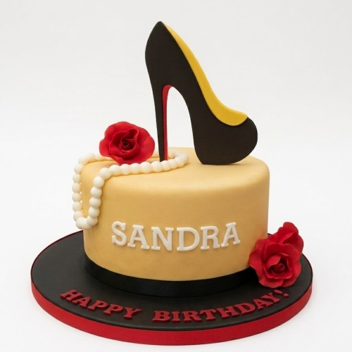 Round yellow birthday cake with black and yellow high heel shoe, white pearl necklace, and red roses.