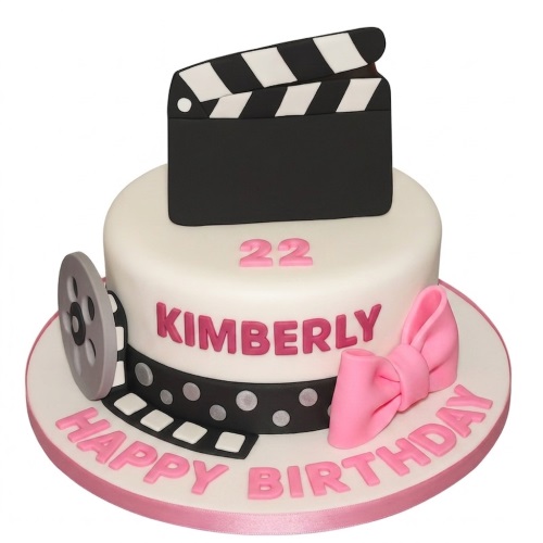 White single tier movie theme birthday cake with clapperboard, film reel, and pink bow.