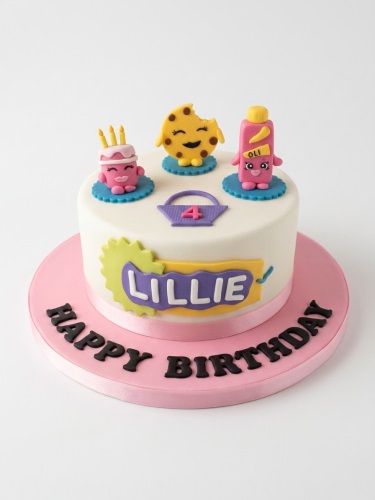 White round birthday cake with Shopkins characters, a purple basket with custom age, and a personalised name banner.