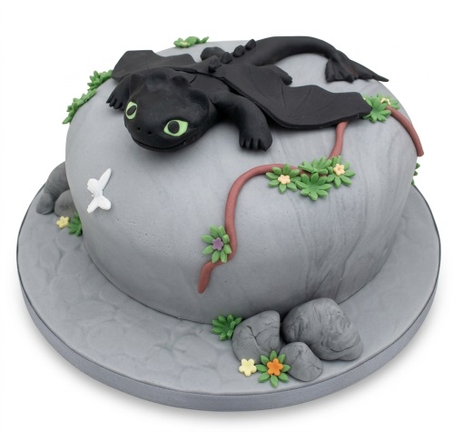 Single-tier grey rock-themed birthday cake with a black dragon figure, green leaves, and small flowers.