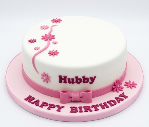 Round white cake with pink floral decorations, ribbon, bow, and 'Happy Birthday' message.