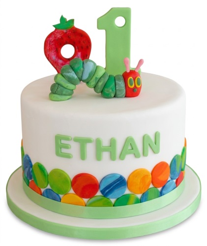 White fondant cake with The Very Hungry Caterpillar, a red strawberry, green number one, and colourful circles.