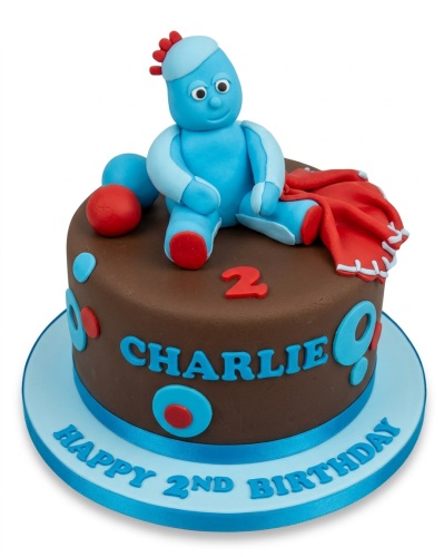 Round brown fondant cake with Igglepiggle figurine, red blanket, blue and red polka dots, custom age number, and personalised name.