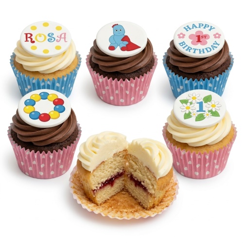 Assortment of 1st birthday cupcakes with character, floral '1', and personalised name toppers on vanilla and chocolate sponges.