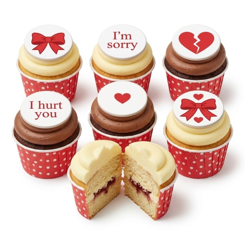 A selection of cupcakes with white toppers featuring red bows, red hearts, a broken heart, and 'I'm sorry' messages.