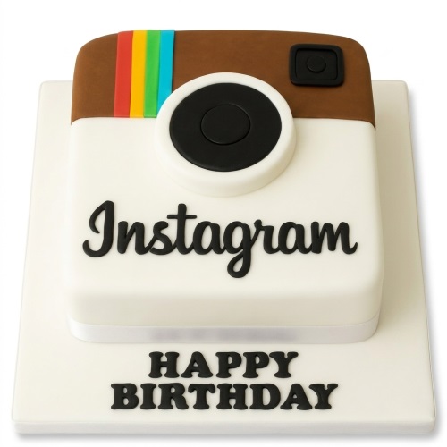 Square Instagram theme birthday cake with brown top, white base, rainbow stripe, black camera lens, and 'Instagram' text. 'HAPPY BIRTHDAY' written on the cake board.