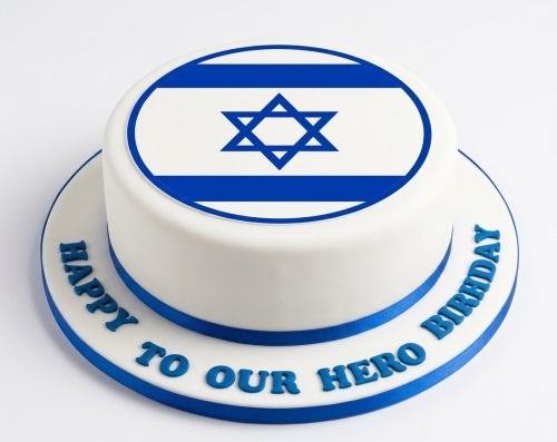 Round white cake with Israel flag on top and blue ribbon, personalised message on board.