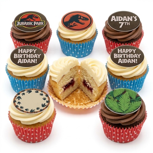 A selection of Jurassic Park themed birthday cupcakes with dinosaur logos, jungle leaves, and custom age/name toppers on cream and chocolate frosting.
