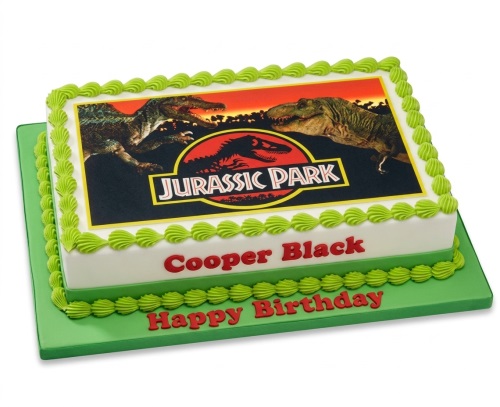 Rectangular white cake with green piping, featuring an edible image of Jurassic Park dinosaurs and logo, with a custom name and 'Happy Birthday' message.