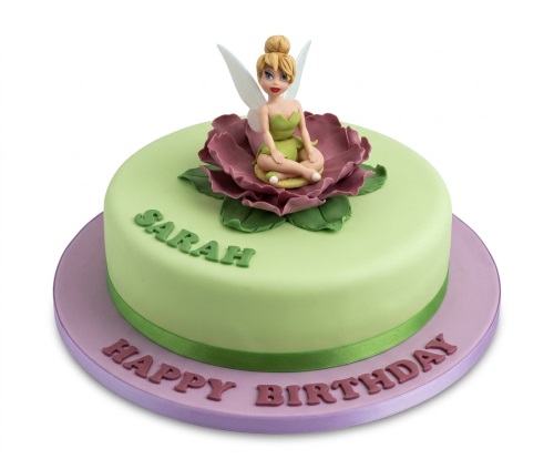 Round light green cake with a Tinkerbell figurine on a purple flower, green ribbon, and a personalised message.