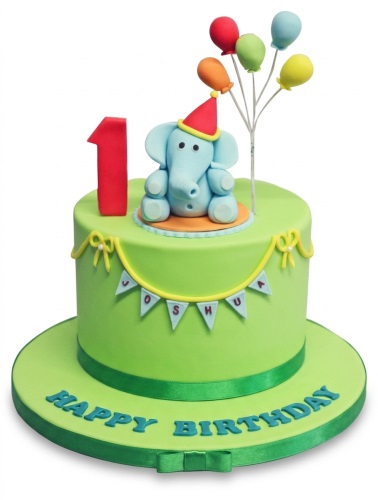 Green fondant cake with blue elephant, red number 1 topper, colourful balloons, and "Happy Birthday" text.