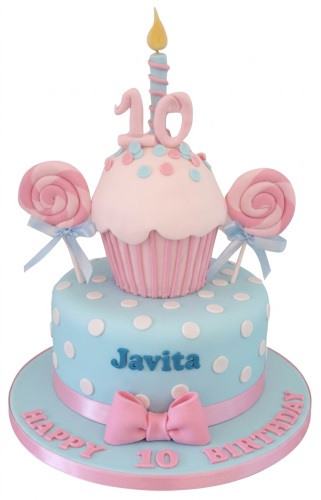 Two-tier pink and blue polka dot girls birthday cake with cupcake, lollipops, and custom age topper.