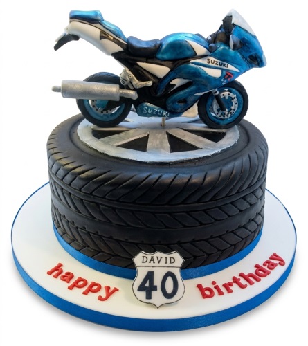 Blue and white motorbike cake on a black tyre-shaped cake with a custom age sign and 'happy birthday' message.