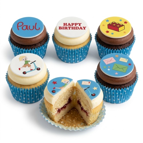 Assortment of kids birthday cupcakes with scooter, Lego brick, and Happy Birthday toppers in blue polka dot wrappers.
