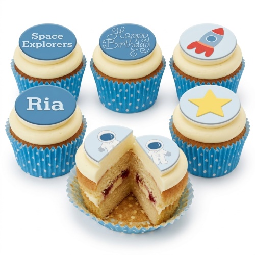 Vanilla cupcakes with blue polka dot wrappers and space-themed edible toppers including rockets, stars, astronauts, and custom messages.