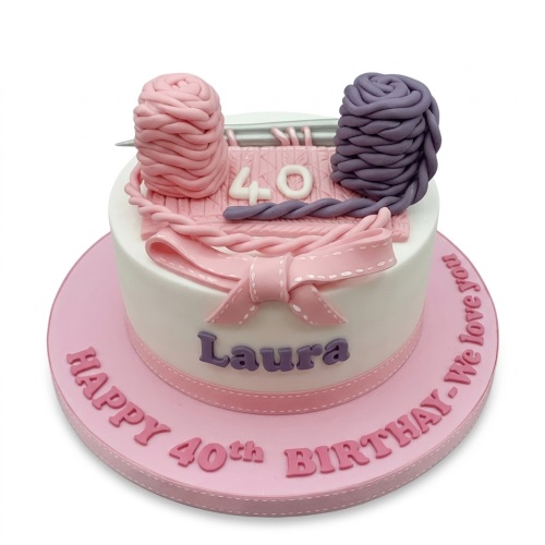Round white birthday cake with pink and purple yarn balls, knitting needles, and a custom age topper.