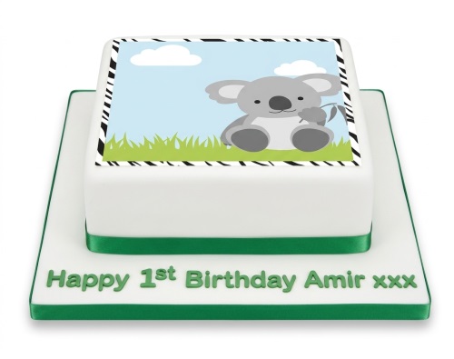 Square white cake with an edible image of a cute koala, green ribbon, and personalised 1st birthday message.