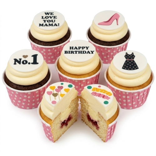 Selection of birthday cupcakes with white frosting, pink polka dot wrappers, and various toppers including a pink high heel, black dress, 'Happy Birthday', 'No.1', and 'We Love You Mama!' messages. One cupcake is cut open revealing a jam filling.