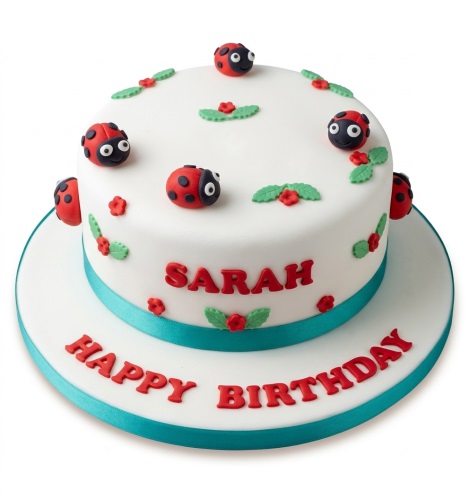 Two-tier white ladybug birthday cake with red ladybirds, green leaves, and a teal ribbon.
