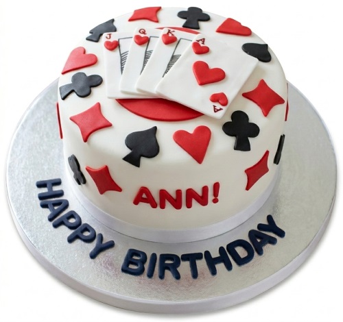 Round white birthday cake decorated with red and black playing card suits and edible playing cards, with 'Happy Birthday' on the board.