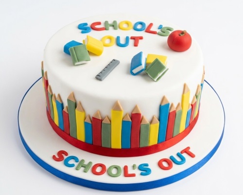 Round white cake with "SCHOOL'S OUT" message, decorated with colourful edible pencils, books, ruler, and a red apple.
