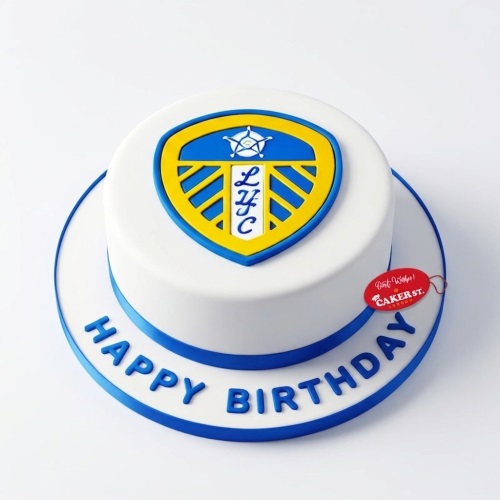 Round white football birthday cake with a blue and yellow Leeds United FC crest on top and a blue 'Happy Birthday' message.