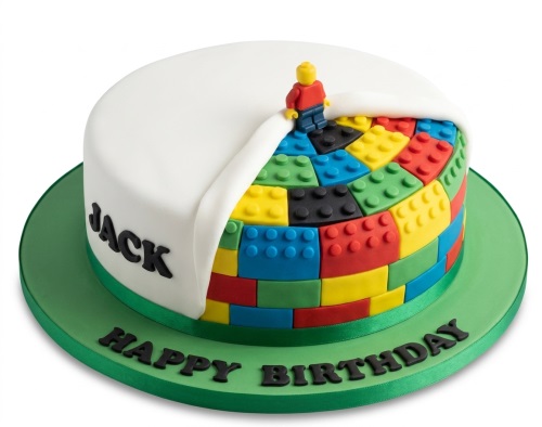 Round white birthday cake with colourful building blocks and a small figure, green base.