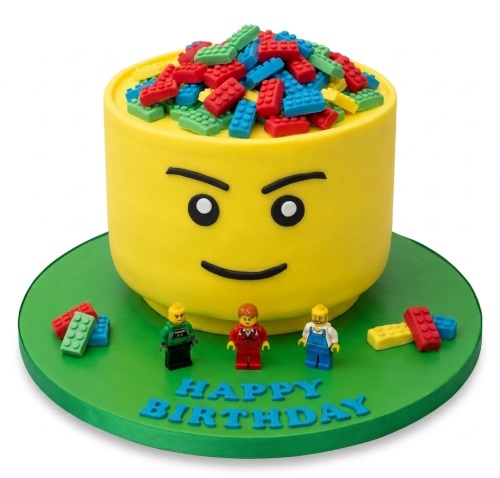 Yellow round cake shaped like a Lego head, topped with red, blue, and green edible Lego bricks, with minifigures on a green board.